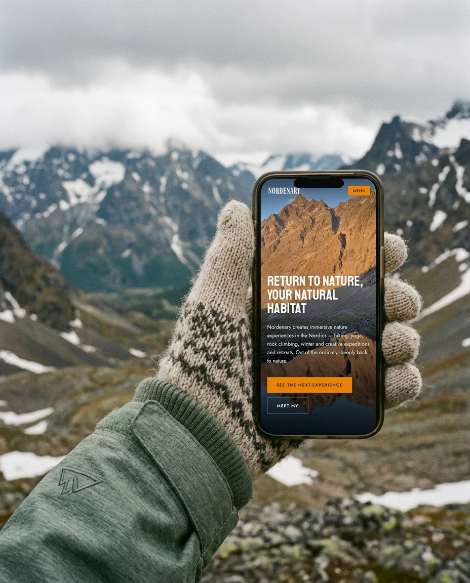 The Nordenary website on a phone held in a mitten, with snowy mountains behind