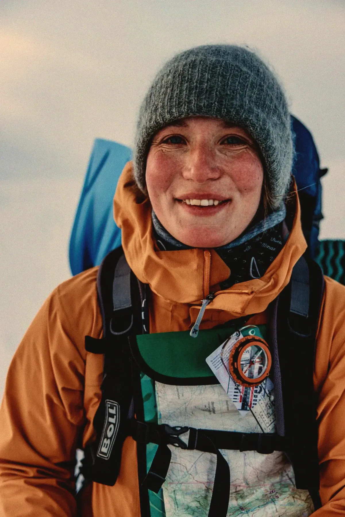 My Myrenberg smiling in a wool hat and orange jacket, with map and compass, on a mountain expedition